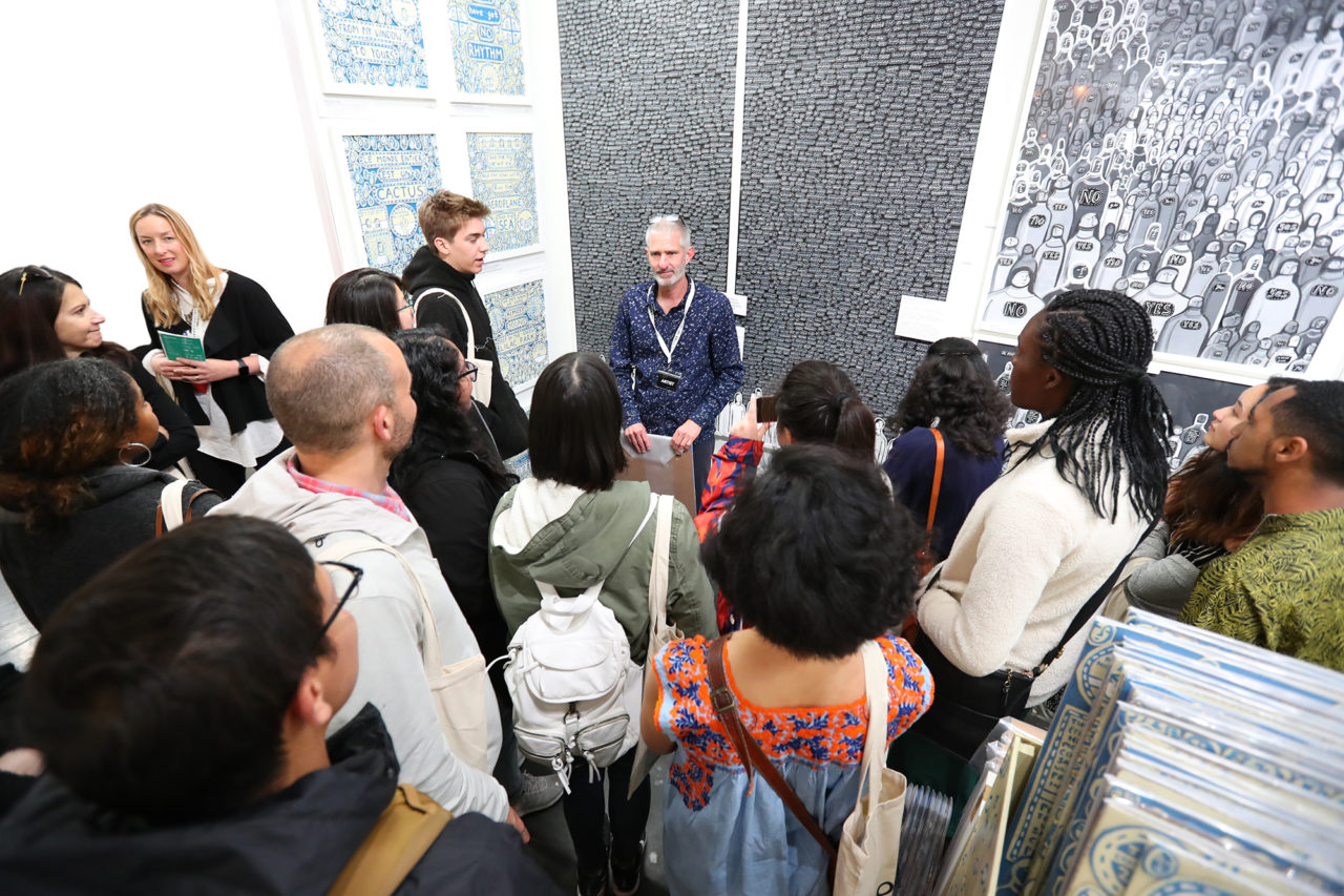A group from Stanford University standing in front of the two tall Reconstitution panels, listening to a talk.